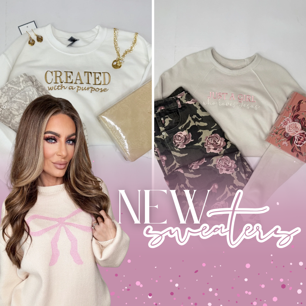 Woman wearing a white sweater with pink accents, surrounded by sweaters with floral designs and text | New Sweaters | Bloom West Boutique | Houma, LA