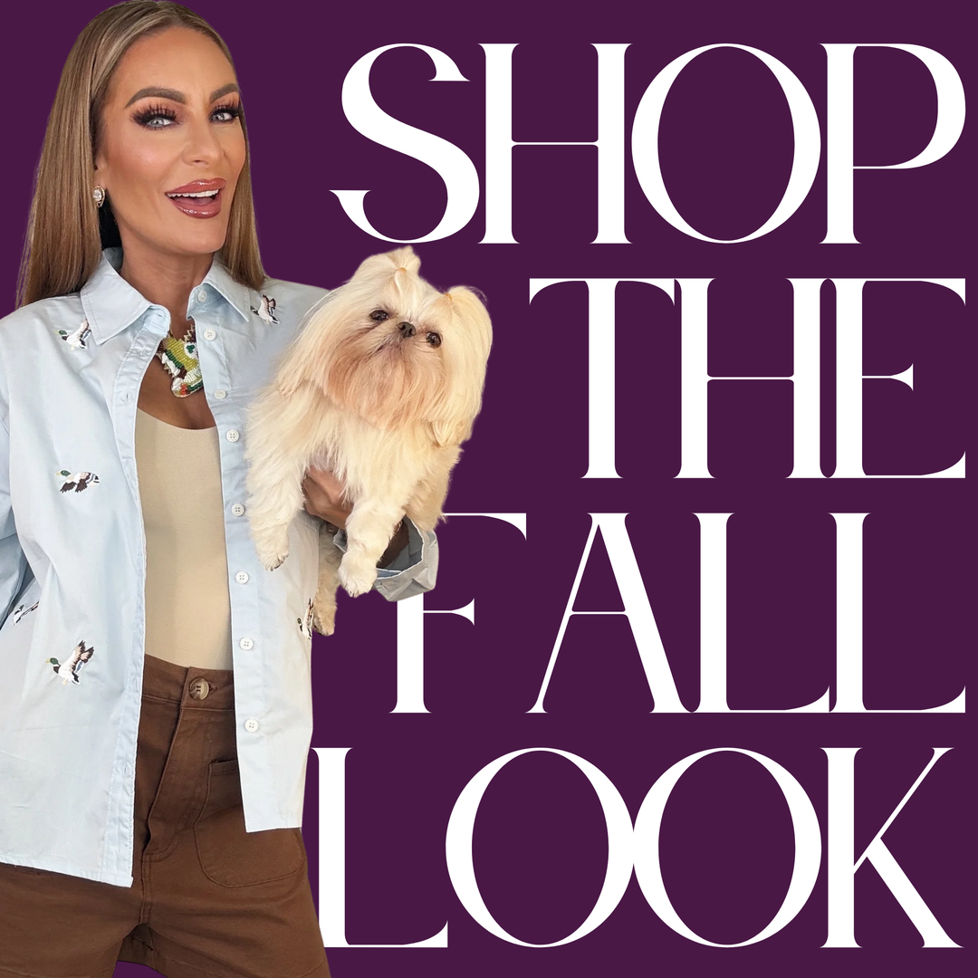 A woman holding a small fluffy cream dog, wearing a light blue embroidered button-up shirt over a beige top and brown pants, set against a dark purple background with large white text reading 'SHOP THE FALL LOOK' | Bloom West Boutique | Houma, LA